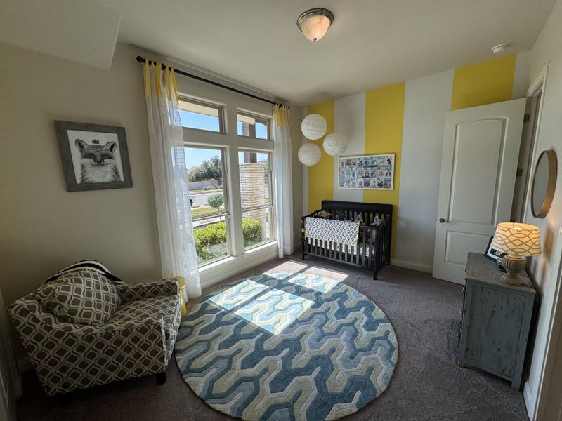 A cozy nursery with yellow accent walls, bright windows, a stylish armchair, and a patterned rug.