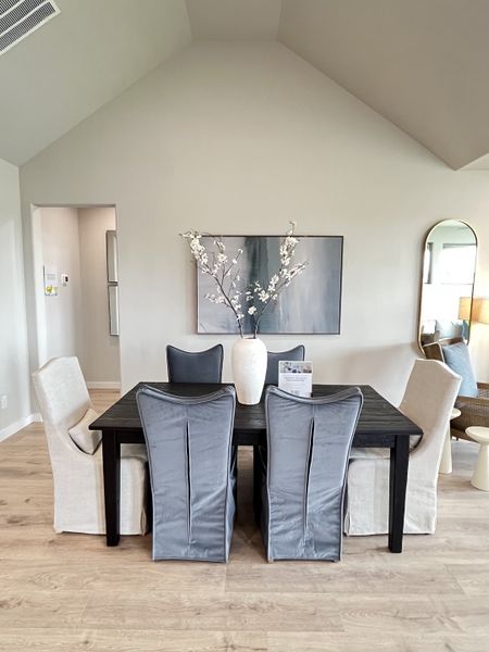 A modern dining room with a vaulted ceiling, elegant gray and white chairs, and a stylish vase centerpiece.