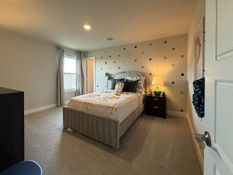 A cozy bedroom with a playful polka dot accent wall, soft carpeting, and natural light from a large window.