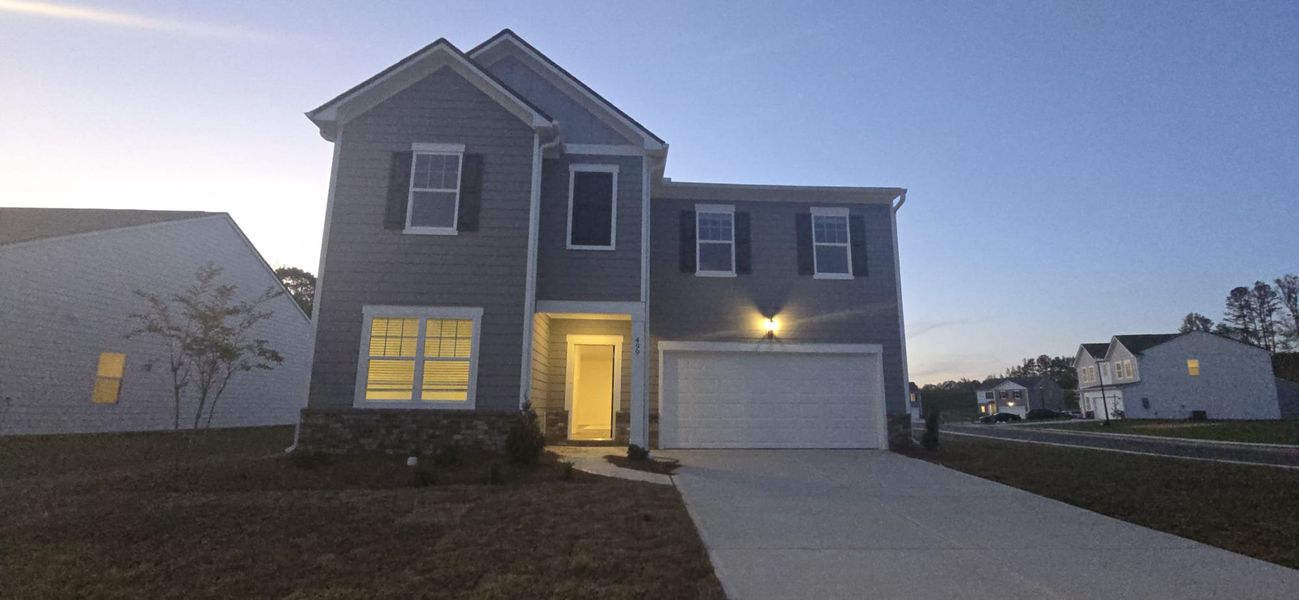 A charming gray home at dusk with illuminated windows in Casteel by Starlight Homes (Bethlehem, GA).
