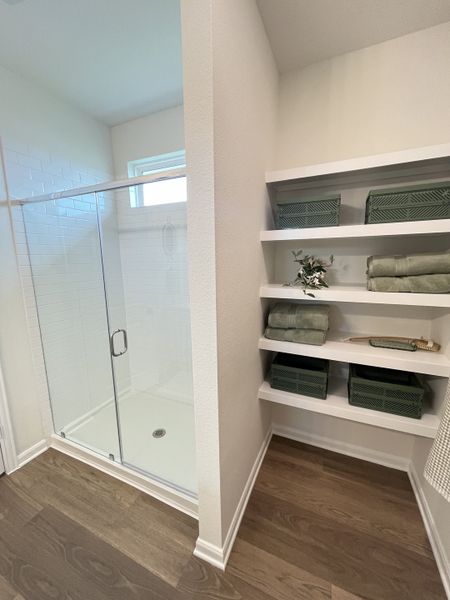 A modern bathroom features an elegant glass shower, spacious shelves, and natural wood flooring for a sleek look.