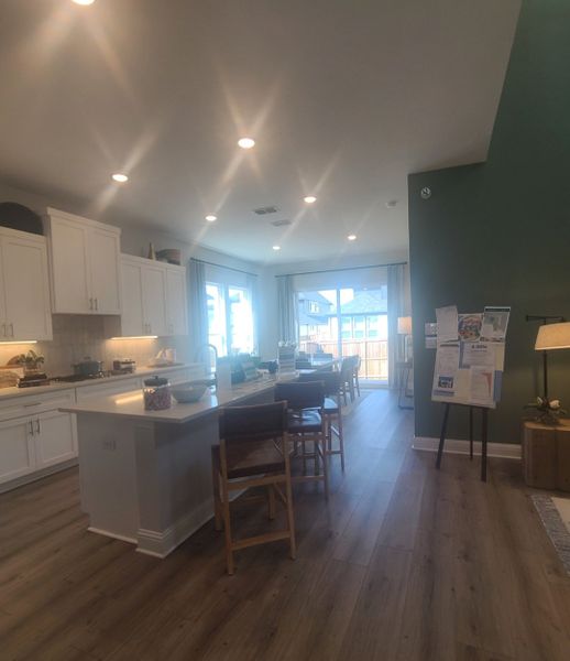 A luminous kitchen and dining area with hardwood floors, an island, and large windows.