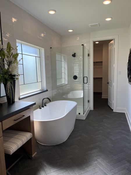 A luxurious bathroom featuring a soaking tub, glass shower, and elegant dark herringbone flooring.