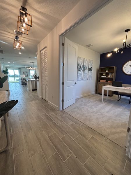 A modern hallway with wood-look tiles, stylish lighting, and an elegant office space featuring a navy accent wall.
