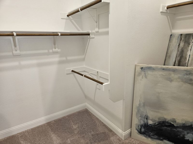 A spacious walk-in closet with wooden rods, plush carpet, and abstract artwork leaning against the wall. A spacious walk-in closet with wooden rods, plush carpet, and abstract artwork leaning against the wall.