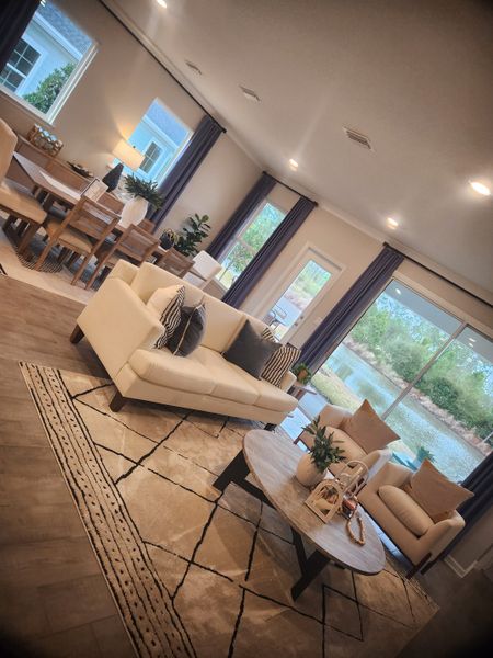 A cozy living and dining area with sleek furniture, large windows, and warm decor, offering a serene view of the outdoors.