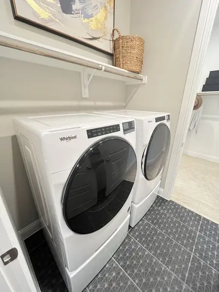A modern laundry room featuring sleek appliances, patterned floor tiles, and stylish shelving with decor accents. A modern laundry room featuring sleek appliances, patterned floor tiles, and stylish shelving with decor accents.