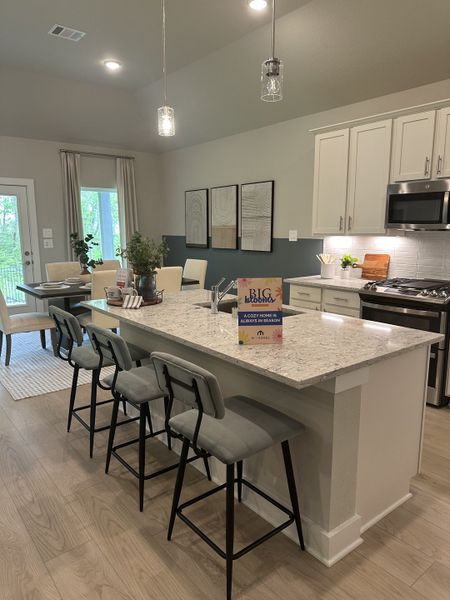A modern kitchen with a large island, barstools, pendant lighting, and stylish artwork on the walls.