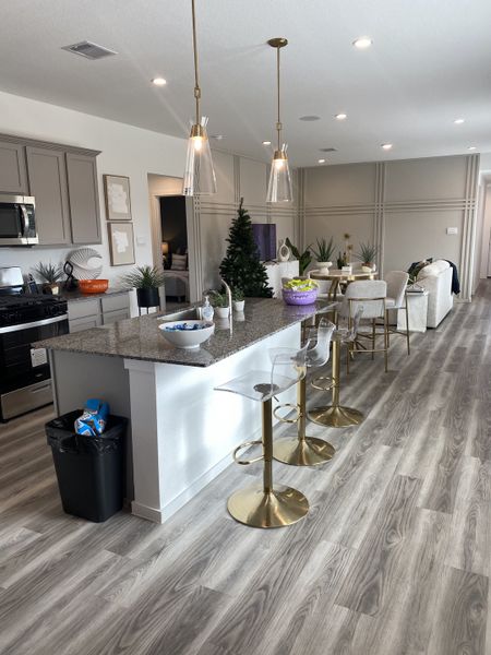 A modern open-concept kitchen with gray cabinets, pendant lighting, and a sleek island with gold barstools.