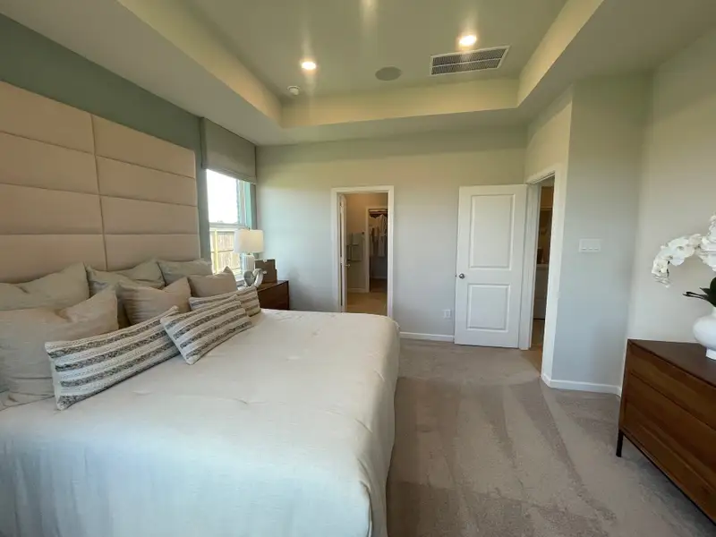 A cozy bedroom featuring a plush bed, neutral tones, layered pillows, and modern furnishings with soft carpet flooring.