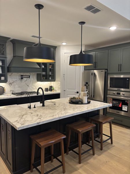 A chic kitchen with a marble island, sleek black lighting, and modern stainless steel appliances. A chic kitchen with a marble island, sleek black lighting, and modern stainless steel appliances.