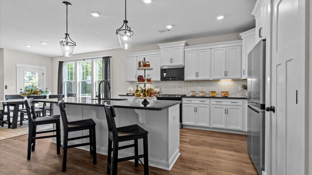 White cabinetry kitchen with modern pendant lighting over extended island with granite countertops by DRB Homes