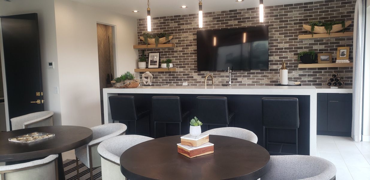 A modern kitchen with a brick accent wall, sleek bar seating, open shelves, and stylish pendant lights.