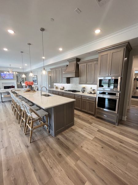 A spacious kitchen with a large island, elegant pendant lights, gray cabinetry, and wood flooring. A spacious kitchen with a large island, elegant pendant lights, gray cabinetry, and wood flooring.
