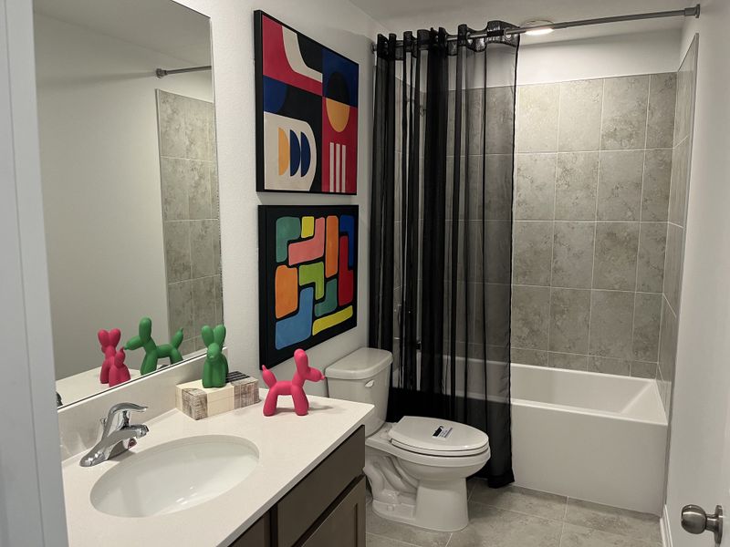 A modern bathroom with abstract art, gray-tiled tub, sleek vanity, and playful decor accents.
