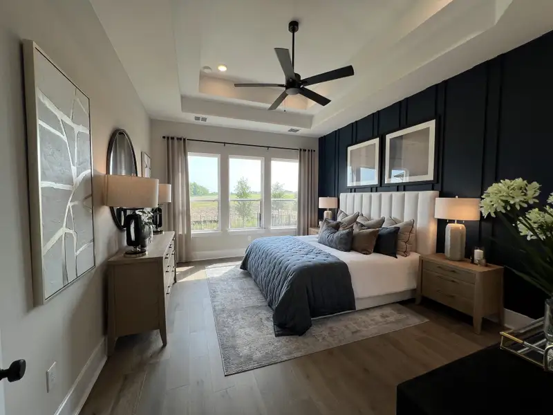 A sophisticated bedroom featuring a modern fan, elegant decor, large windows, and plush bedding with contrasting accent walls.