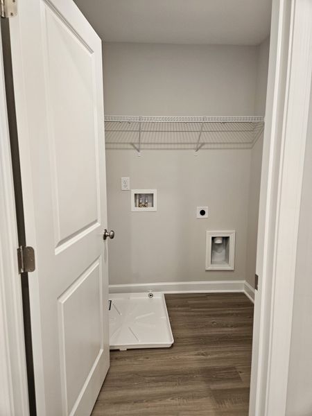 A convenient laundry room with wood-look flooring, wall shelving, and dedicated space for appliances.