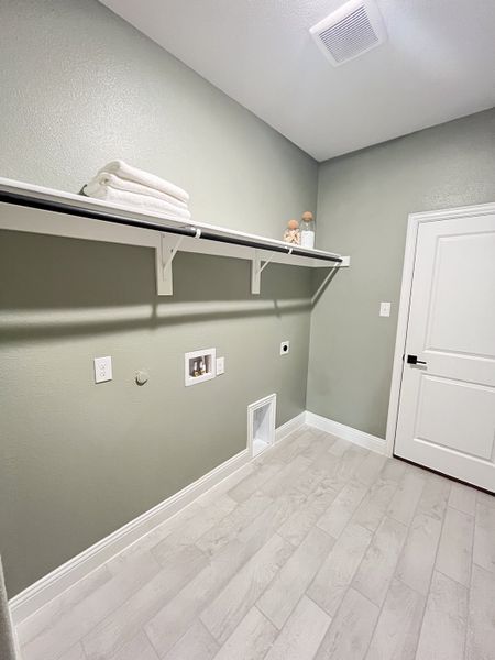 A spacious laundry room with soft gray walls and modern tile flooring, featuring a built-in shelf and ample utility space.