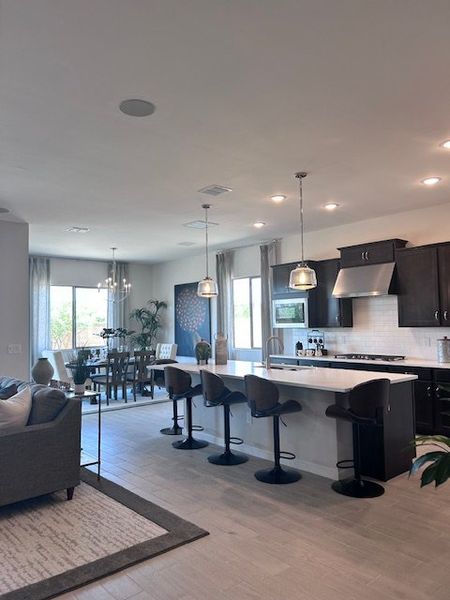 A modern open-concept kitchen and dining area with sleek dark cabinets, pendant lighting, and large windows. A modern open-concept kitchen and dining area with sleek dark cabinets, pendant lighting, and large windows.