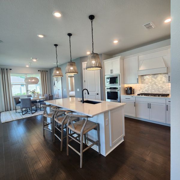 A bright kitchen featuring a large island, pendant lights, sleek white cabinetry, and a dining area with modern decor.
