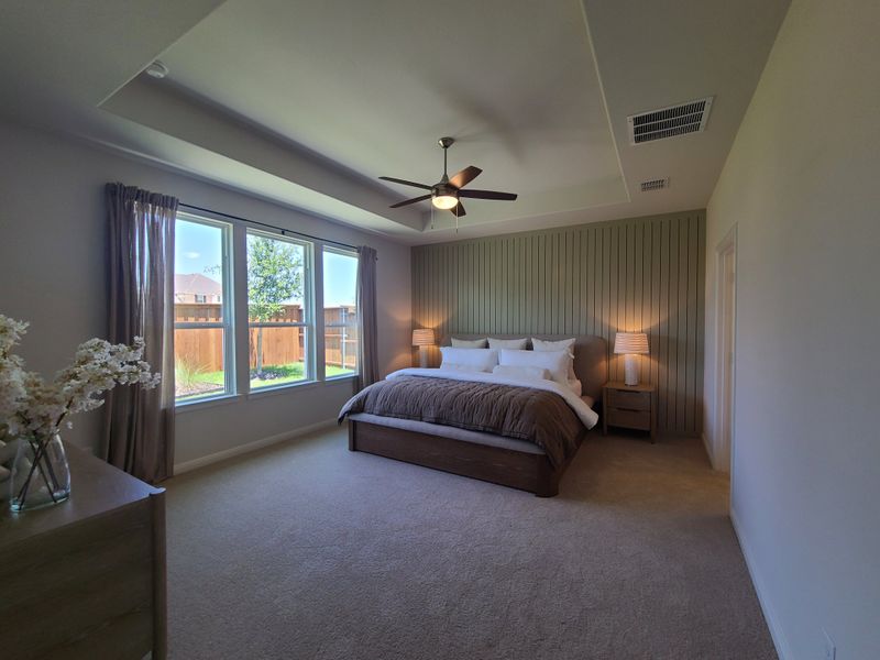 A spacious bedroom featuring large windows, cozy bedding, textured accent wall, and soft lighting for a relaxing ambiance.