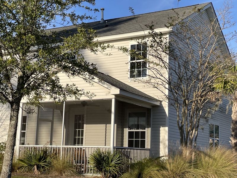 A charming beige two-story home with a cozy porch in High Point at Foxbank by Dream Finders Homes (Moncks Corner, SC).