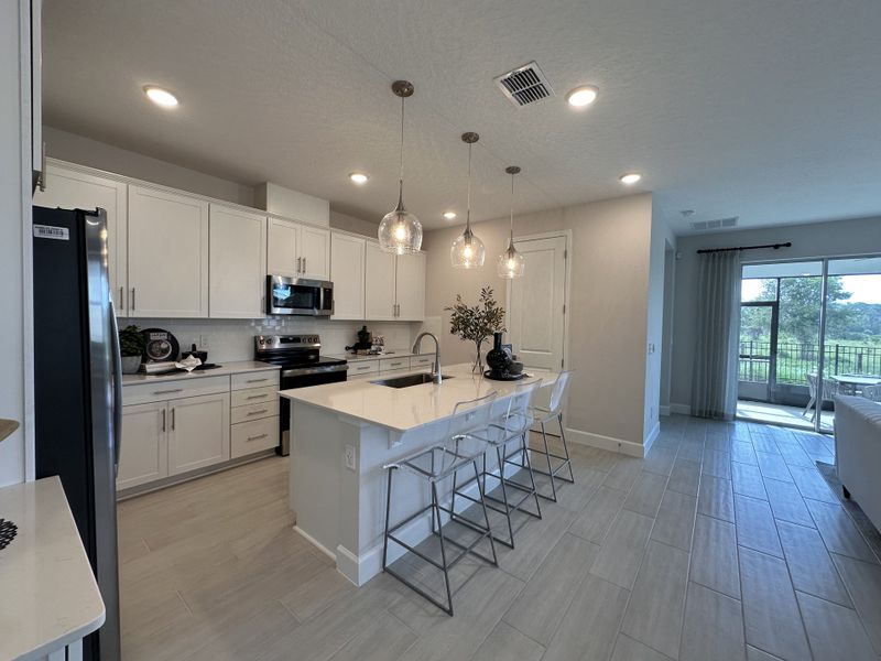 A modern kitchen with sleek white cabinetry, an island with pendant lighting, and expansive views through glass doors.