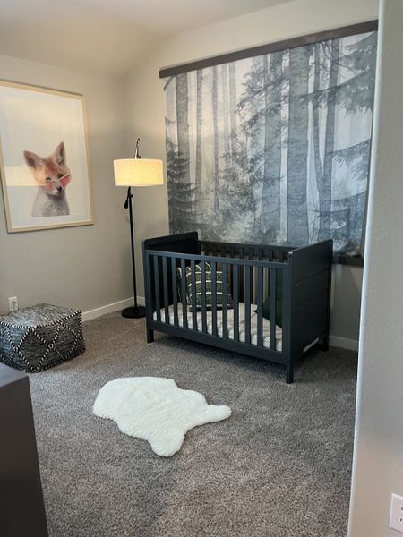 A cozy nursery with a dark crib, fox artwork, forest-themed wallpaper, and a plush white rug.