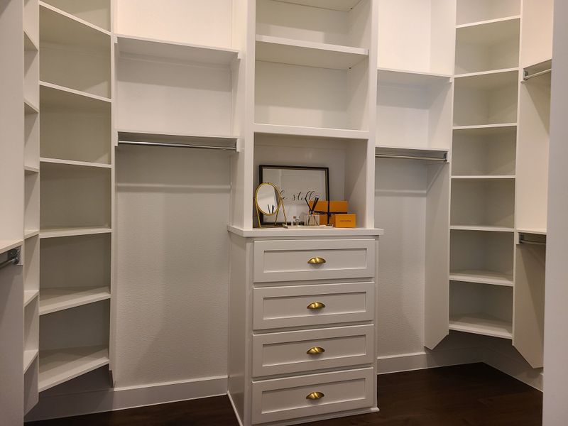 A spacious walk-in closet with white shelving, a central dresser, and elegant accents for a modern, organized feel. A spacious walk-in closet with white shelving, a central dresser, and elegant accents for a modern, organized feel.