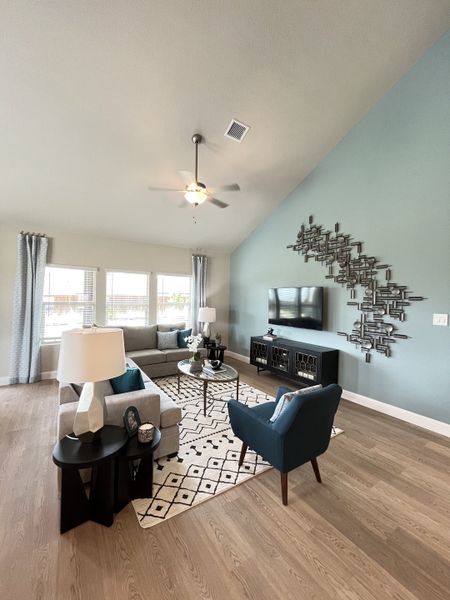 A modern living room with light wood floors, gray sofa, blue accent wall, stylish decor, and a unique metal art piece.