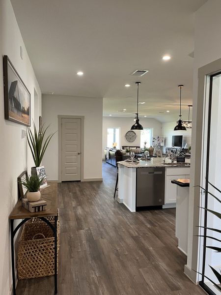 A modern open kitchen with wood floors, sleek pendant lights, and a cozy entryway, offering a welcoming atmosphere.