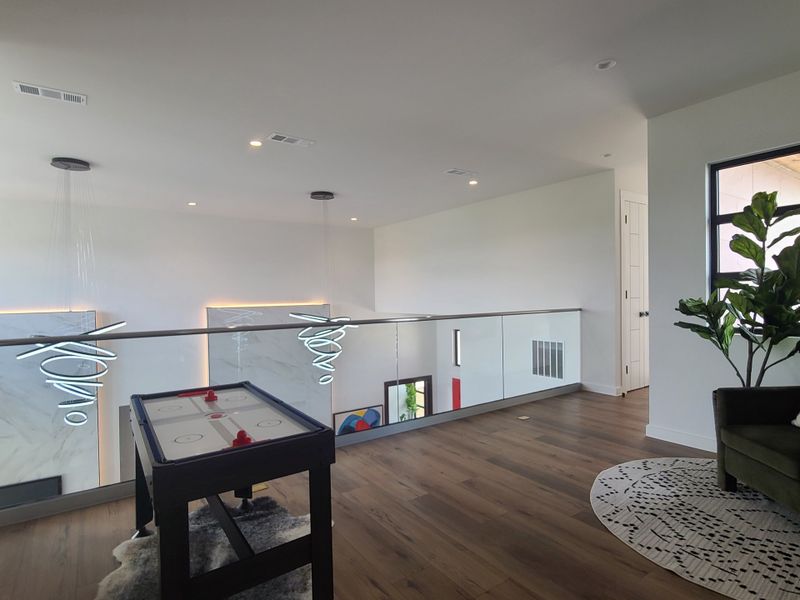 A modern loft space with sleek lighting, a glass railing, and an air hockey table, complemented by a cozy corner with a plant.