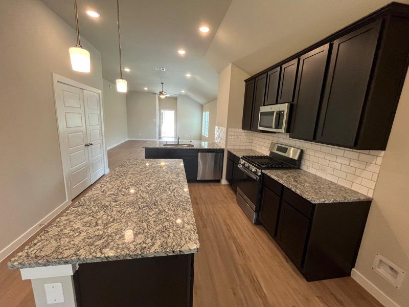 A sleek kitchen with granite countertops, dark cabinets, stainless steel appliances, and a spacious open layout.