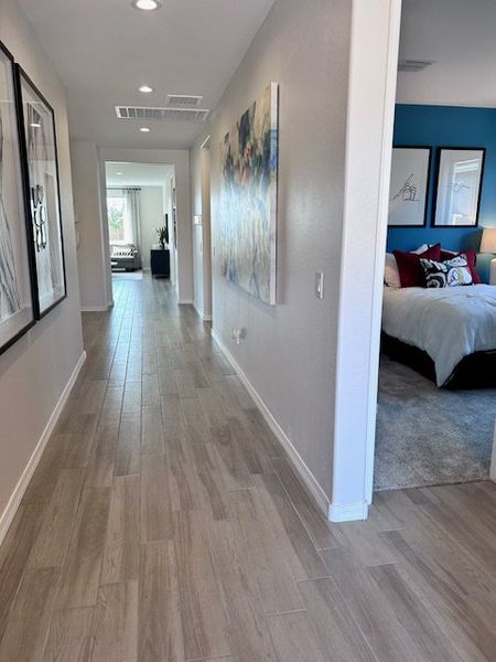 A modern hallway with sleek wood flooring and contemporary art, leading to a bright bedroom with cozy decor.