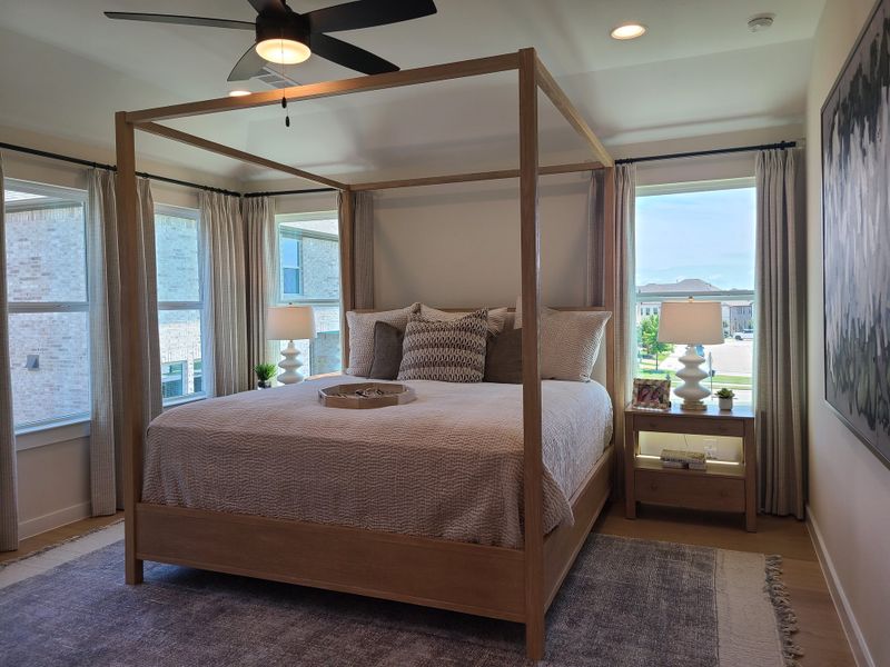 A cozy bedroom featuring a wooden canopy bed, elegant lamps, and large windows draped with light curtains. A cozy bedroom featuring a wooden canopy bed, elegant lamps, and large windows draped with light curtains.