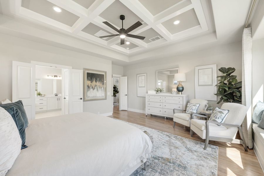 Large master bedroom with coffered ceiling, ceiling fan, hardwood floors, and ensuite bathroom access