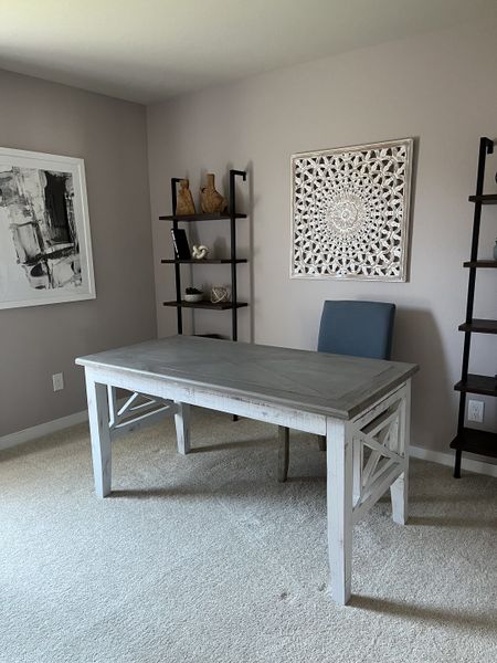 A modern home office with neutral walls, a rustic desk, elegant artwork, and minimalist shelving.