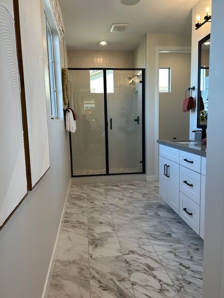 A modern bathroom with marble flooring, a glass-enclosed shower, and a sleek white vanity with black accents.