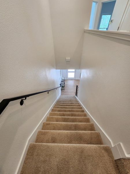 A cozy carpeted staircase with sleek black handrail leading to a bright, airy hallway and wooden flooring.