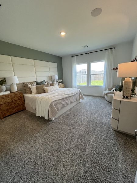 A serene bedroom featuring plush carpeting, a cozy bed with neutral bedding, and ample natural light through large windows.