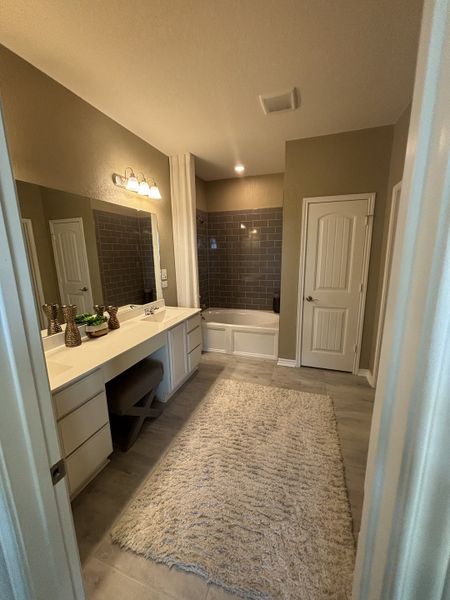 A cozy bathroom featuring a spacious vanity, soft lighting, and a plush rug with a modern tub and gray tiled walls. A cozy bathroom featuring a spacious vanity, soft lighting, and a plush rug with a modern tub and gray tiled walls.