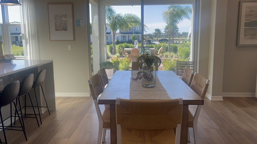 A bright dining area with a wooden table, woven chairs, and large windows overlooking a lush garden.