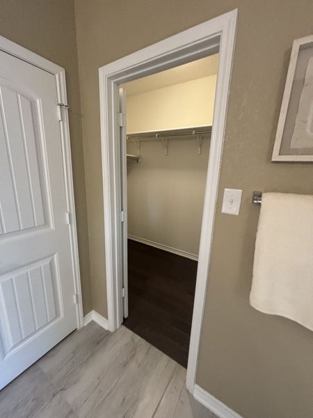 A walk-in closet with ample shelving, accessible from a tiled room with neutral-toned walls. A walk-in closet with ample shelving, accessible from a tiled room with neutral-toned walls.