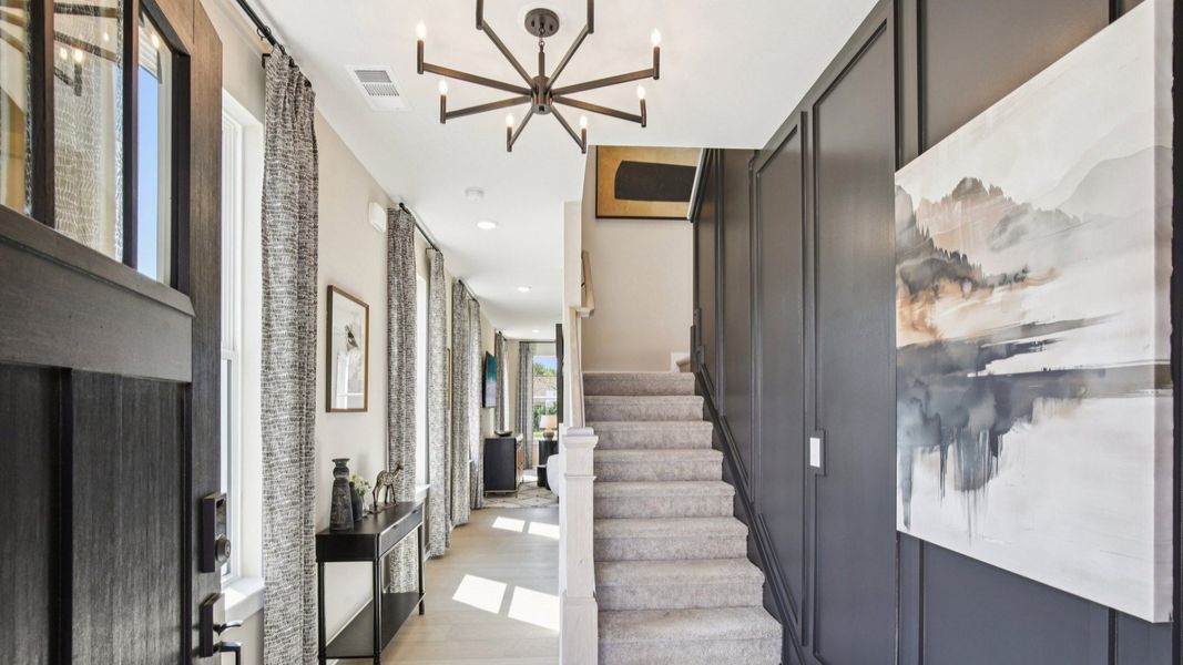 Welcoming entry with accent wall, hallway to gathering room, and stairs to second floor