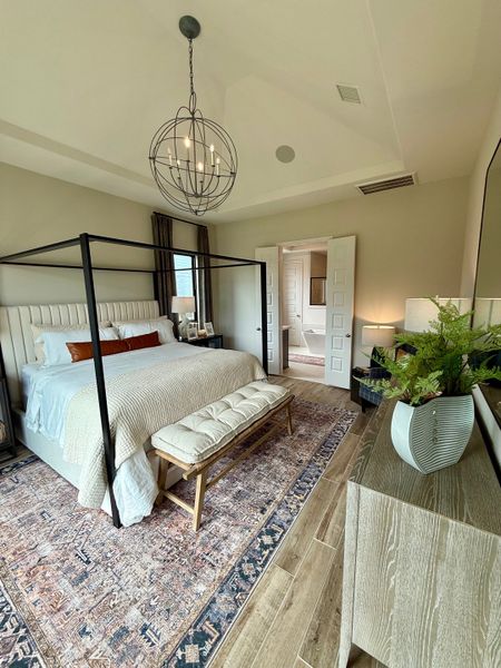 A cozy bedroom featuring a four-poster bed, elegant pendant lighting, and a stylish rug on wooden flooring.