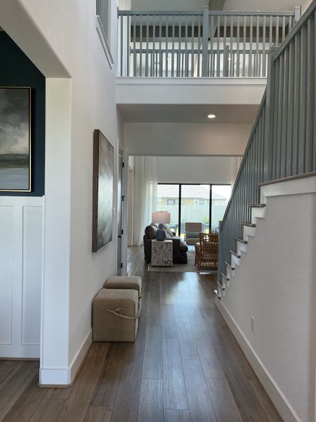 An elegant hallway with light wood flooring, open staircase, and bright living area view, offering a welcoming ambiance.