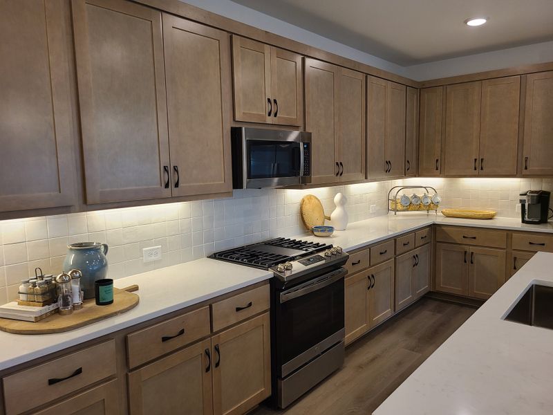 A modern kitchen with sleek wooden cabinets, under-cabinet lighting, and stainless steel appliances.