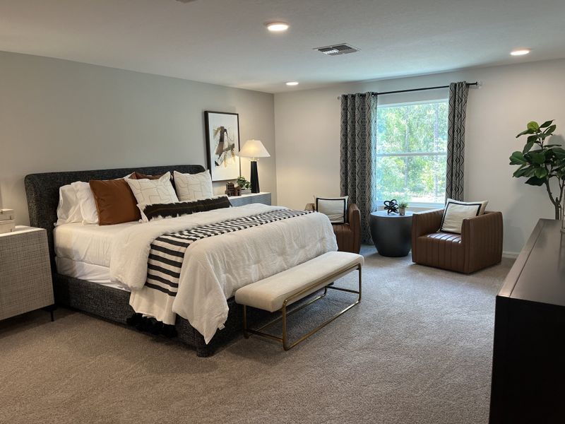 A cozy bedroom with a plush bed, stylish armchairs, and a large window, featuring elegant decor and calming tones.