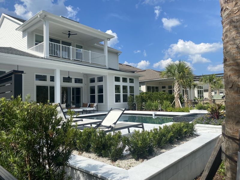 A beautiful white home with a pool and lush landscaping in Reflections At Nocatee by Riverside Homes (Ponte Vedra Beach, FL).