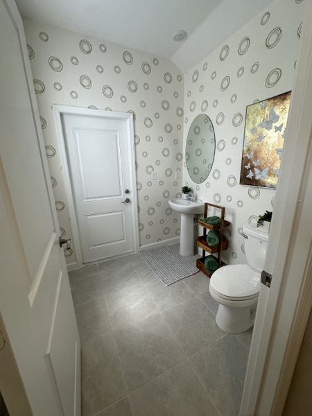 A modern bathroom with circular patterned wallpaper, an oval mirror, and sleek fixtures, creating a fresh, stylish ambiance.